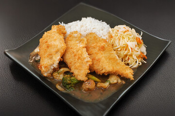 Oriental dish: crispy panko-coated chicken with vegetables, salad and rice on a plate stands on the table.