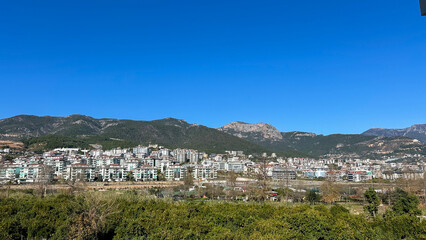 Obraz premium Cityscape With Orange Groves And Mountain Range Under Clear Blue Sky, Captured In Daylight, Represents Nature And Urban Harmony, Perfect For Real Estate, Tourism, Or Environmental Campaigns.