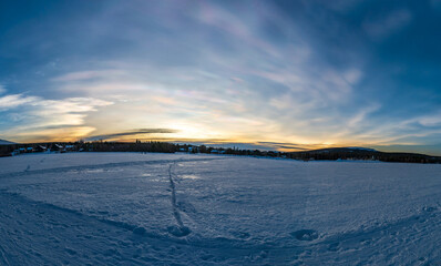 Beautiful winter sunset with rare nacreous clouds known as rainbow clouds over frozen lake Akaslompolo in Finnish Lapland.