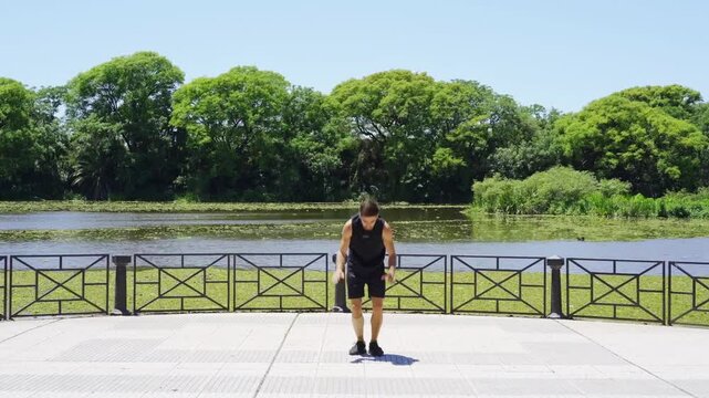 Young Latino man doing burpees by the lakeside in a city park