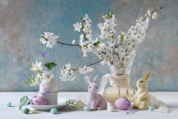 Easter still life with bouquets of spring flowers, blossoming branches of cherry plum, bird cherry, anemones, decorative rabbits and eggs on the table