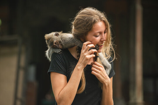Smiling tourist woman interacting with monkeys at a sacred monkey forest temple in Bali.