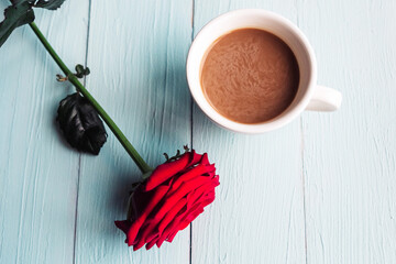 Red rose and coffee cup on wooden table, top view