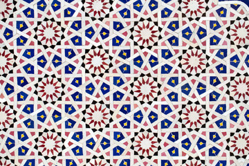 A detailed Islamic geometric mosaic featuring vibrant colors and symmetrical patterns. The design showcases traditional arabesque motifs with star shapes and interwoven lines
