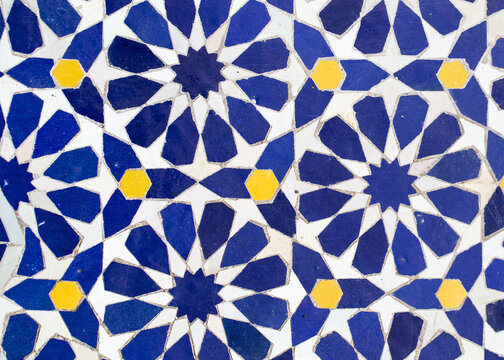 A detailed Islamic geometric mosaic featuring vibrant colors and symmetrical patterns. The design showcases traditional arabesque motifs with star shapes and interwoven lines