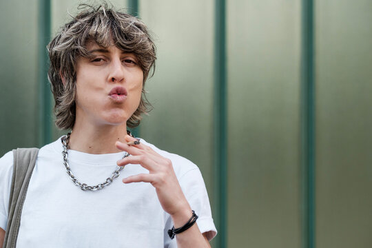 Young person smoking a cigarette and pursing lips outdoors
