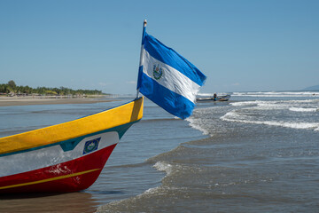 Fishing boat with Salvadoran flag at the wide sandy beach in small village during low tide. Sunny day , blue sky. El Cuco, El Salvador.