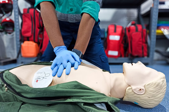 Close-up of middle-aged Asian male hands performing cardiopulmonary resuscitation (CPR) on a training dummy. Vital techniques include defibrillation, chest compressions, and maintaining the airway.