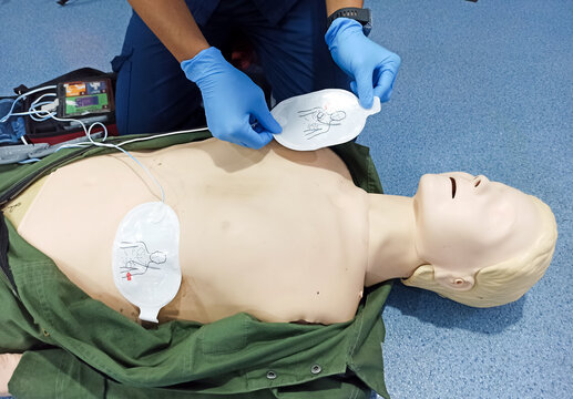cardiac resuscitation techniques, partial view of professional paramedic applying defibrillator pads on CPR manikin, high angle view, health care and life-saving techniques concept
