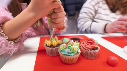 Young girl decorating cupcakes during a baking class preparing muffins and cupcake for birthday...