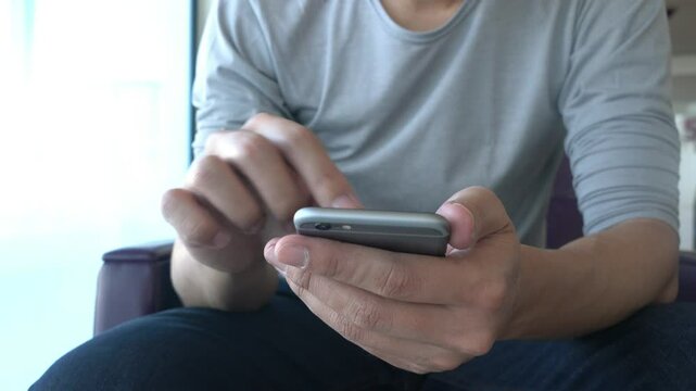 A man is using his cell phone while sitting in a chair. Concept of relaxation and leisure, as the man is focused on his phone rather than his surroundings