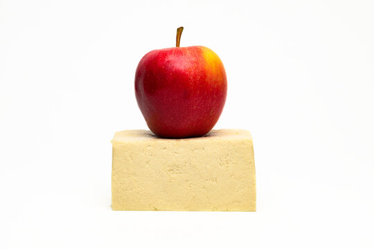 A red apple on top of a block of tofu against a white backround