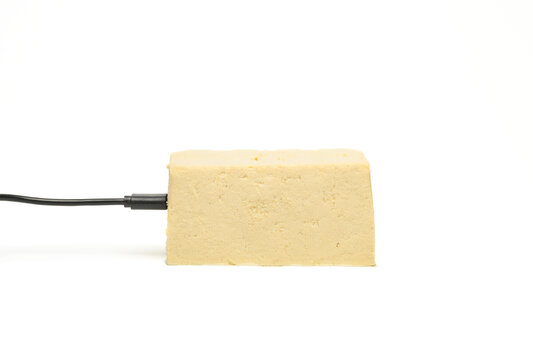 A block of tofu with a power cabled attached to the side against a white background
