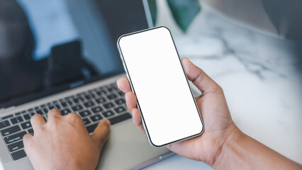 Cell phone white screen mockup, Human hand holding mobile phone with blank screen while working at coffee shop, Businessman using smartphone, Social media advertisement, Design creative work space.