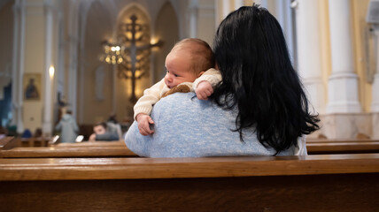 A woman holds a baby boy and sits on a bench in a Catholic church.