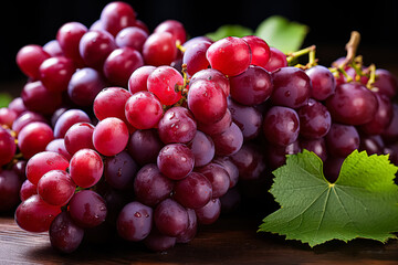 Fototapeta premium Bunch of red grapes with green leaves on top. The grapes are wet and shiny. Concept of freshness and abundance