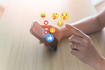 Social media concepts include exchange of ideas, socializing through the internet, technology, and social networking. A woman uses a mobile phone to send emojis to her friends while relaxing at home.