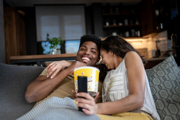 A young couple watching a horror movie at home. The woman looks frightened or grossed out, while...