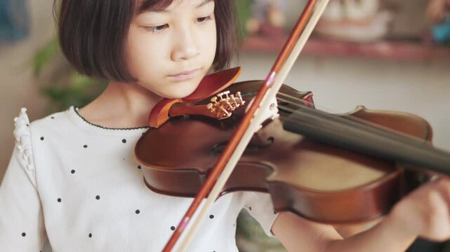 Asian girl passionately plays the violin, demonstrating focus and dedication during a music lesson. Her precise movements and deep concentration highlight her growing talent as a young musician. 