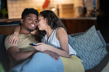 A loving couple cuddles under a cozy blanket on the couch, watching TV together at night in a...