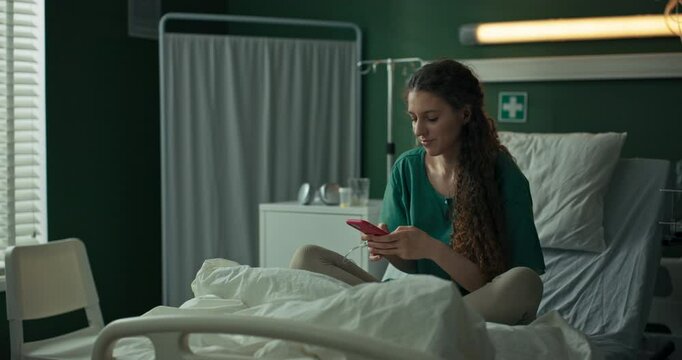 Young patient sits on her hospital bed, focused on her phone as she types a message.