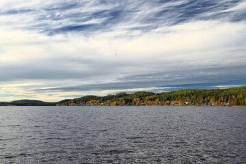 Shoreline reflecting trees and sky, with distant homes nestled in a calm rural landscape at Jarvtrask in northern Sweden