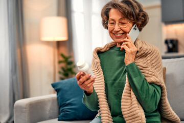 A beautiful elderly woman in a green sweater and knitted blanket is sitting on the sofa at home,...