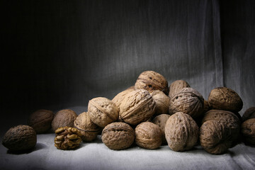 Many unpeeled walnuts piled in a pile lie on a table covered with fabric