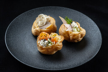 Indulge in gourmet, Asianinspired bites beautifully presented on an elegant plate. Delicious profiteroles filled with fish, pate, onions. Three profiteroles with different fillings lay side by side.