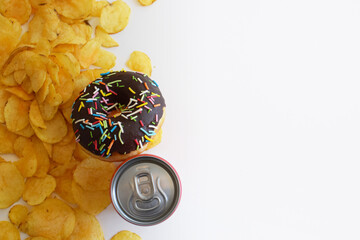 Junk food meal on white background. Red soda or cola can, doughnut, chips. Sweet glazed chocolate donut and lemonade. Fast food restaurant.