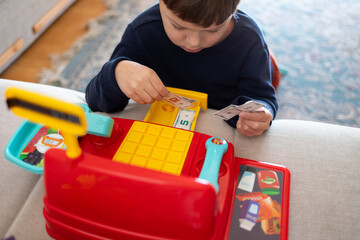 A child plays with a toy cash register and toy money.