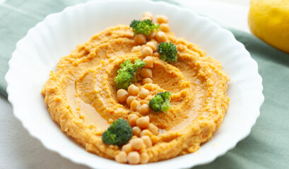 Creamy carrot hummus with chickpeas and broccoli florets, a delicious and healthy snack or appetizer.