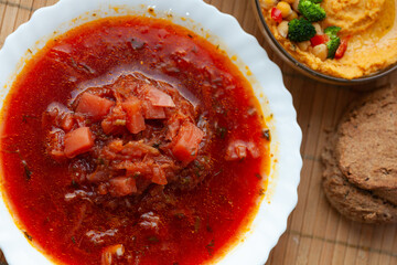 Hearty beet soup with vegetables served with hummus and bread.