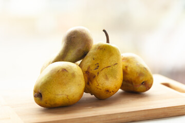 Four ripe pears rest on a light wooden cutting board, bathed in soft, natural light.