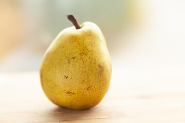 A single ripe pear rests on a light wooden surface, bathed in soft, natural light.  Its skin shows subtle imperfections, adding to its rustic charm.