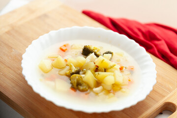 A bowl of hearty vegetable soup, featuring potatoes, carrots, and broccoli, rests on a wooden cutting board.