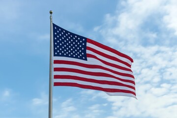 Fototapeta premium A large American flag waving against a backdrop of soft, scattered clouds and a bright blue sky