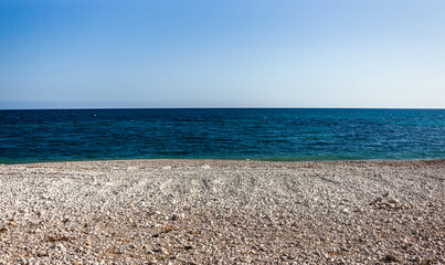 Pebble beach in Costa Blanca, Spain, under a bright sun with a calm sea.