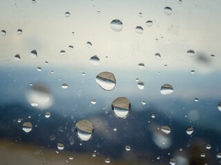 A window with raindrops on it. The raindrops are scattered all over the window, creating a blurry and hazy effect. Scene is calm and peaceful, as the raindrops seem to be falling gently