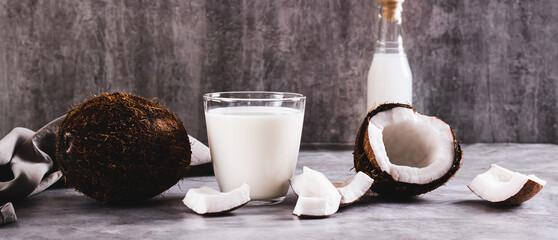 Fresh coconut milk in a glass and coconut pieces on a plate on the table web banner