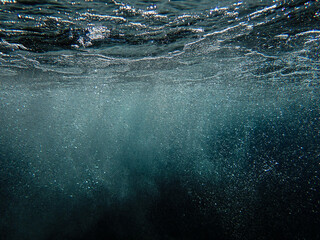 Dark blue ocean surface seen from underwater. Abstract waves underwater and rays of sunlight...
