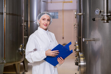 Female Quality Control Inspector Smiling While Checking Wine Tanks in a Modern Winery