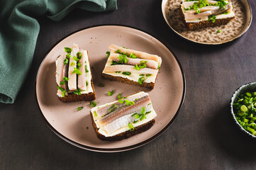 Norwegian smorrebrod made from rye bread, butter and salted herring on a plate on a table