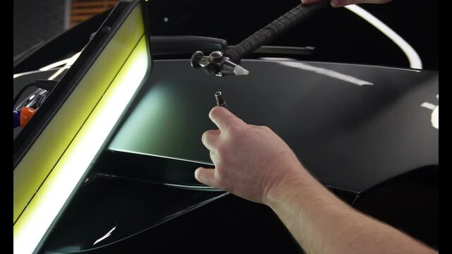A specialist repairs a dent on the car body without painting. Removing dents on the car. PDR technology. Car body repair without painting.	