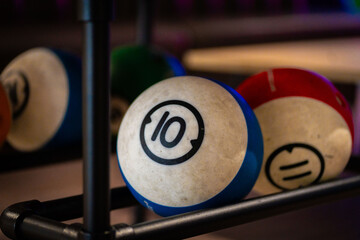 Hand reaching for vibrant bowling ball in colorful, well-lit bowling alley with various balls and blurred background creating dynamic atmosphere