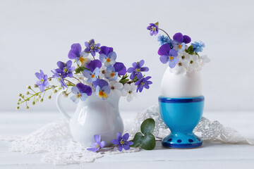 Spring Easter still life with cherry plum flowers, bird cherry, pansies and anemones hepatica in a jug and an egg stand on the table