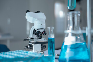Modern microscope stands on table in laboratory with test tubes and flasks containing blue liquid