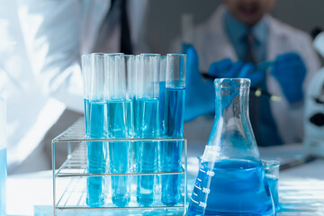 Scientists conducting experiment with blue chemical liquid using test tubes and erlenmeyer flask
