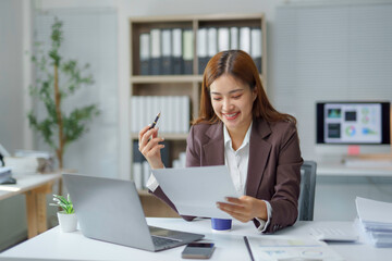 Asian businesswoman smiling and reading a document at office desk