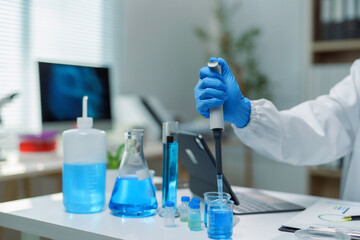Scientist using micropipette adding blue liquid to beaker during experiment in laboratory